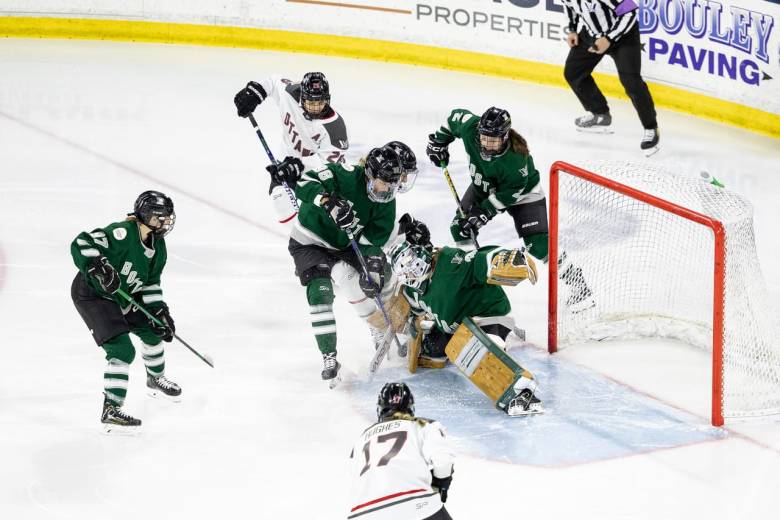 Aerin Frankel, wearing her brown pads, Boston makes, and green home uniform, makes a save through net front chaos.