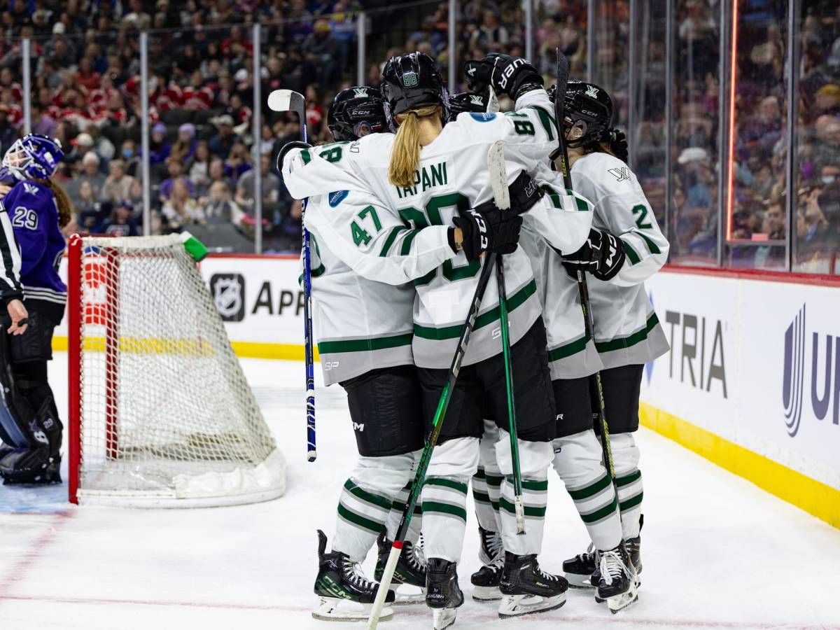 Boston celebrates a goal against Minnesota. They are all in a tight group hug and wearing white away uniforms.
