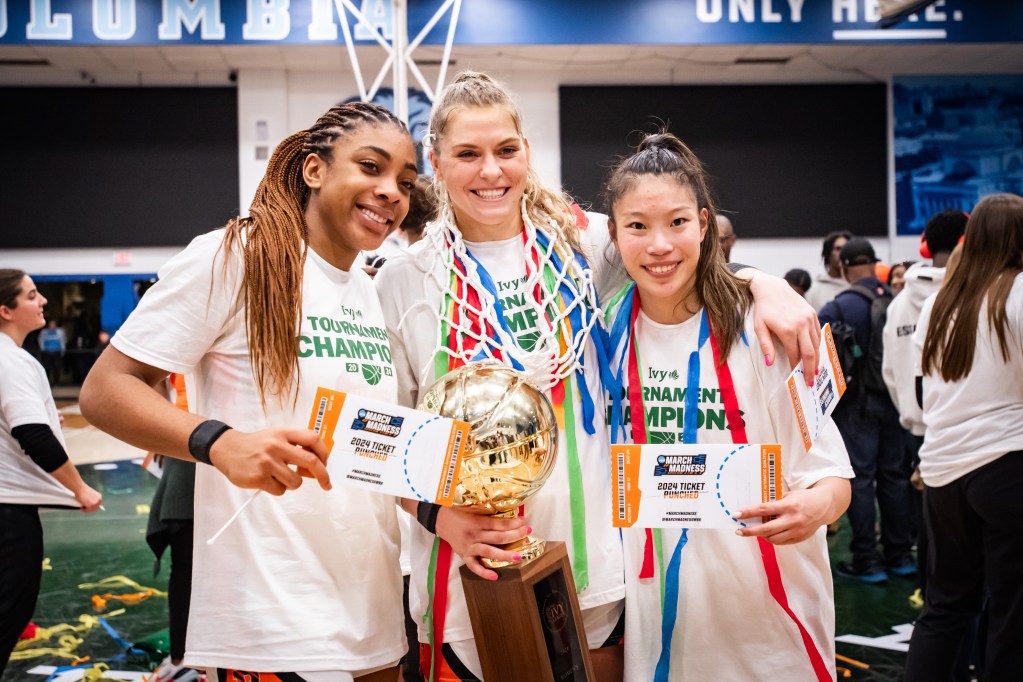 Princeton seniors Chet Nweke, Ellie Mitchell and Kaitlyn Chen smile for a photo with the Ivy League Tournament trophy. Mitchell and Chen have streamers around their necks, and Mitchell has the net that the Tigers cut down also around her neck.
