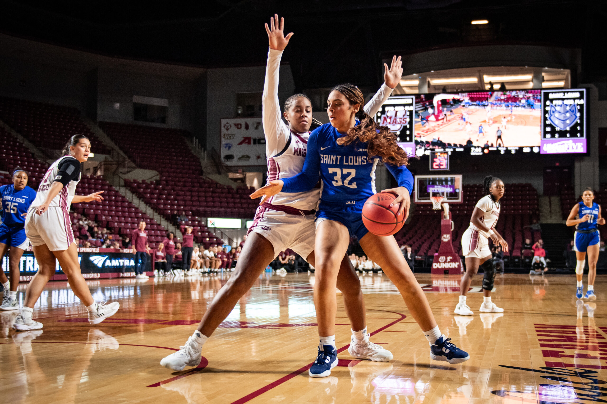 Peyton Kennedy (32) puts her right bicep and upper forearm into the UMass defender while dribbling the ball with her left hand towards the basket.