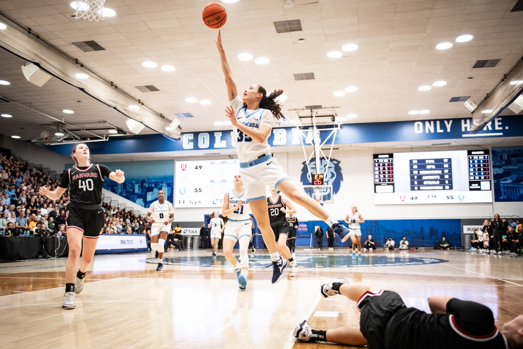 Columbia guard Abbey Hsu shoots an open layup in transition. A Harvard defender is on the floor near the baseline, and another recovers too late to contest Hsu's shot.