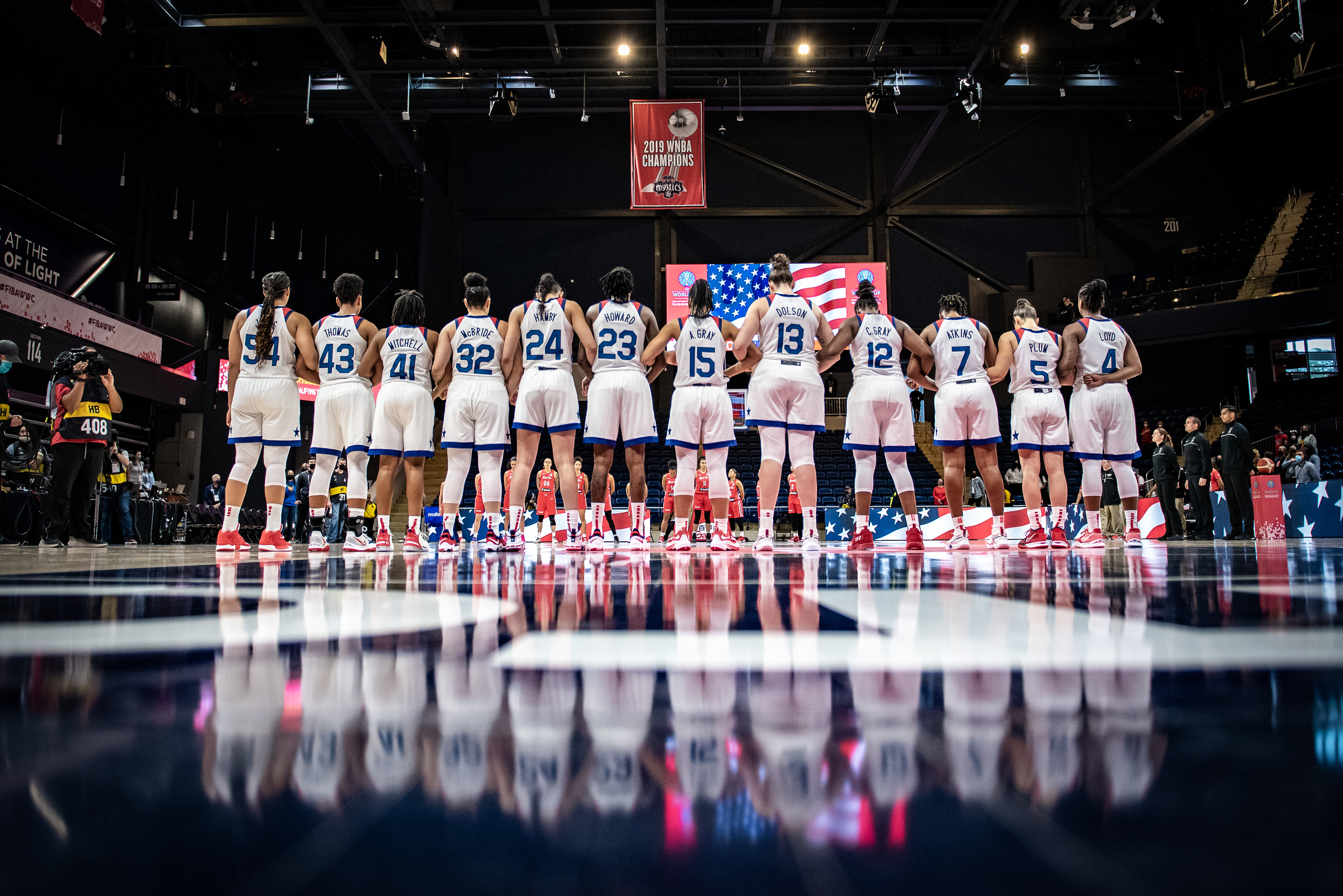 A group of Team USA women’s basketball players stand with their backs toward the camera in 2022.