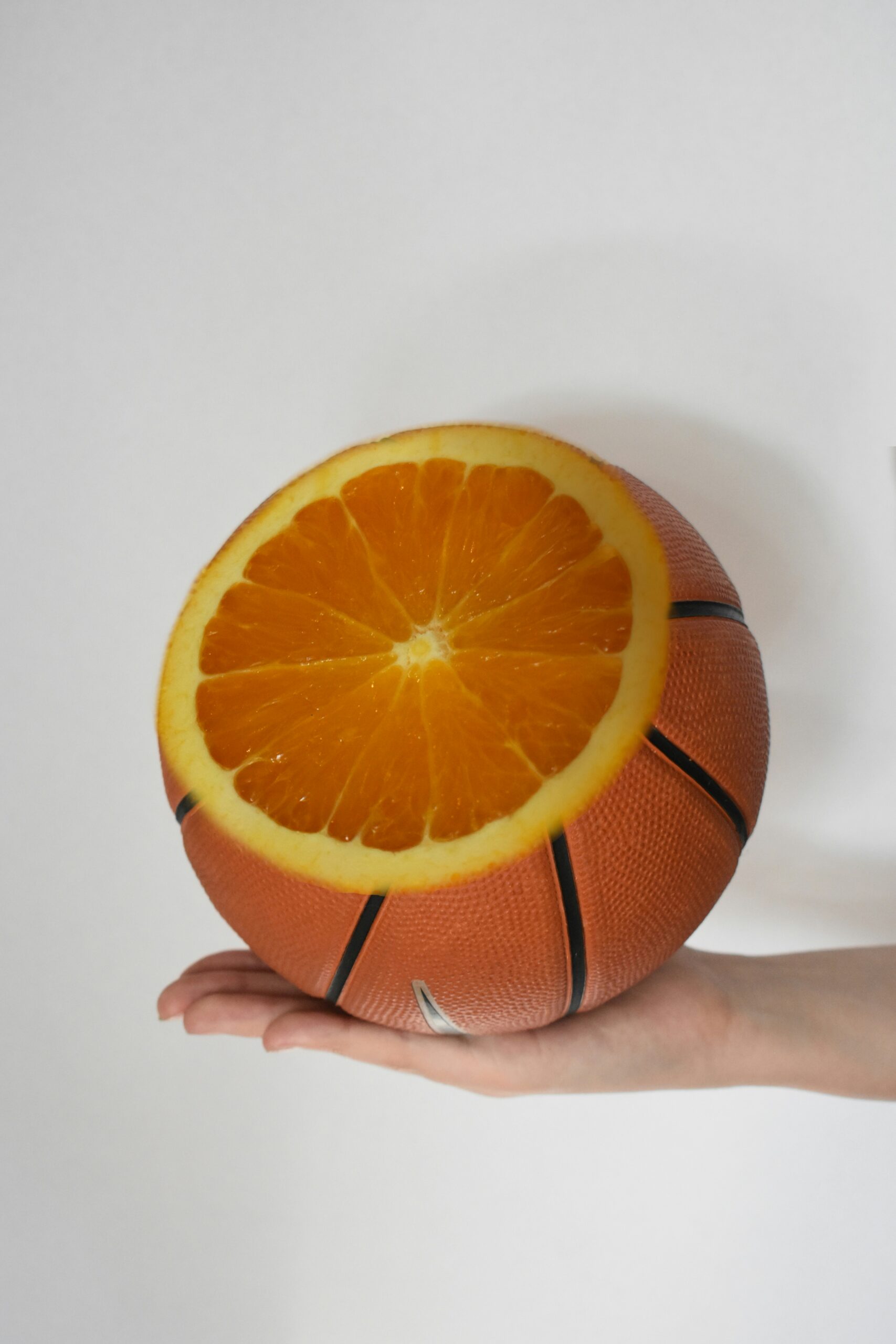 A partially sliced grapefruit being held in the palm of a hand, except the remaining peel looks like a basketball