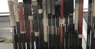 A photo of hockey sticks lined up along the boards, stood up vertically.