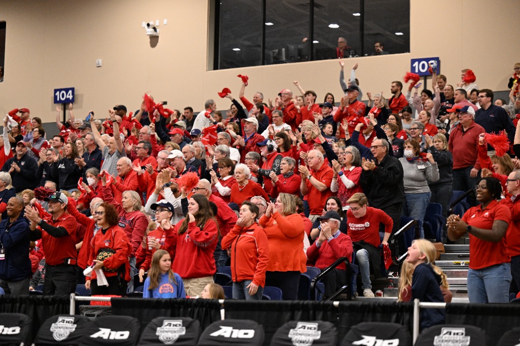 Fans clad in primarily bright red standing while either waving rally towels or applauding.