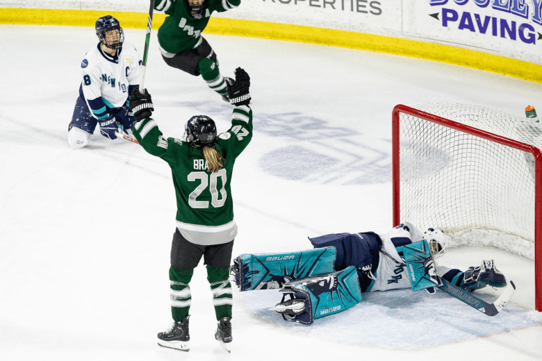 Brandt (in green) raises her arms in celebration. Levy lays on the ice and Zandee-Hart kneels in disbelief (both in white).