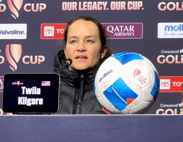 Twila Kilgore sits at a podium with a microphone 