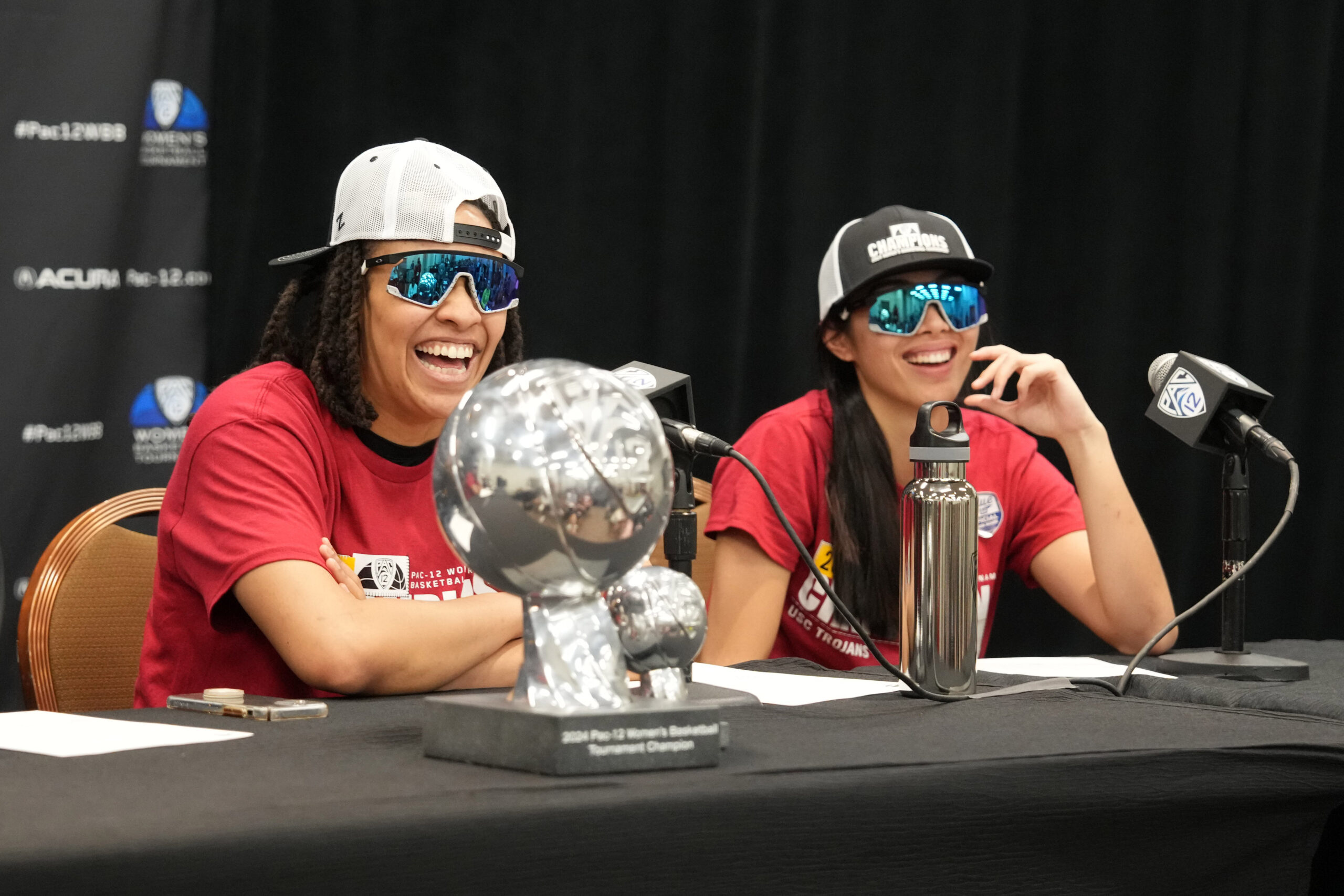 USC guards McKenzie Forbes and Kayla Padilla wear championship hats and T-shirts along with reflective sunglasses as they answer questions in a press conference after winning the Pac-12 Tournament.