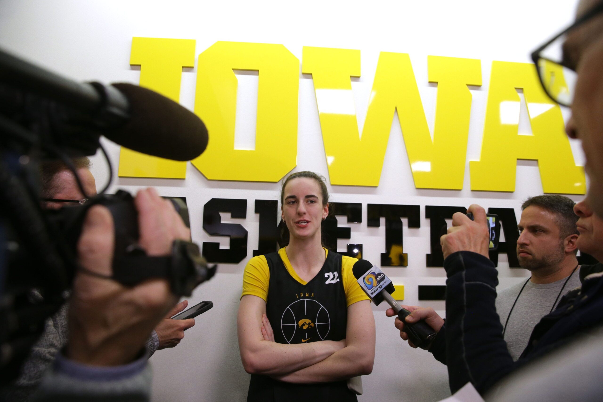 Caitlin Clark, surrounded by reporters with microphones.