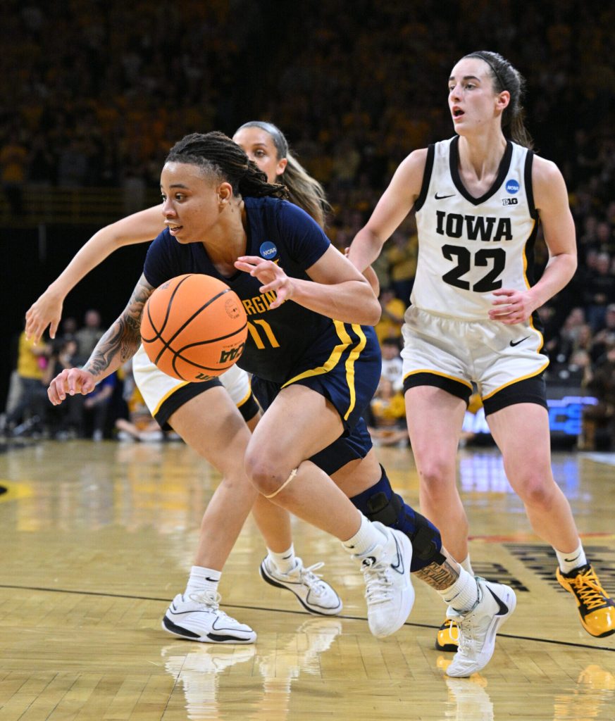 West Virginia guard JJ Quinerly dribbles the ball away from two Iowa players with her left hand.