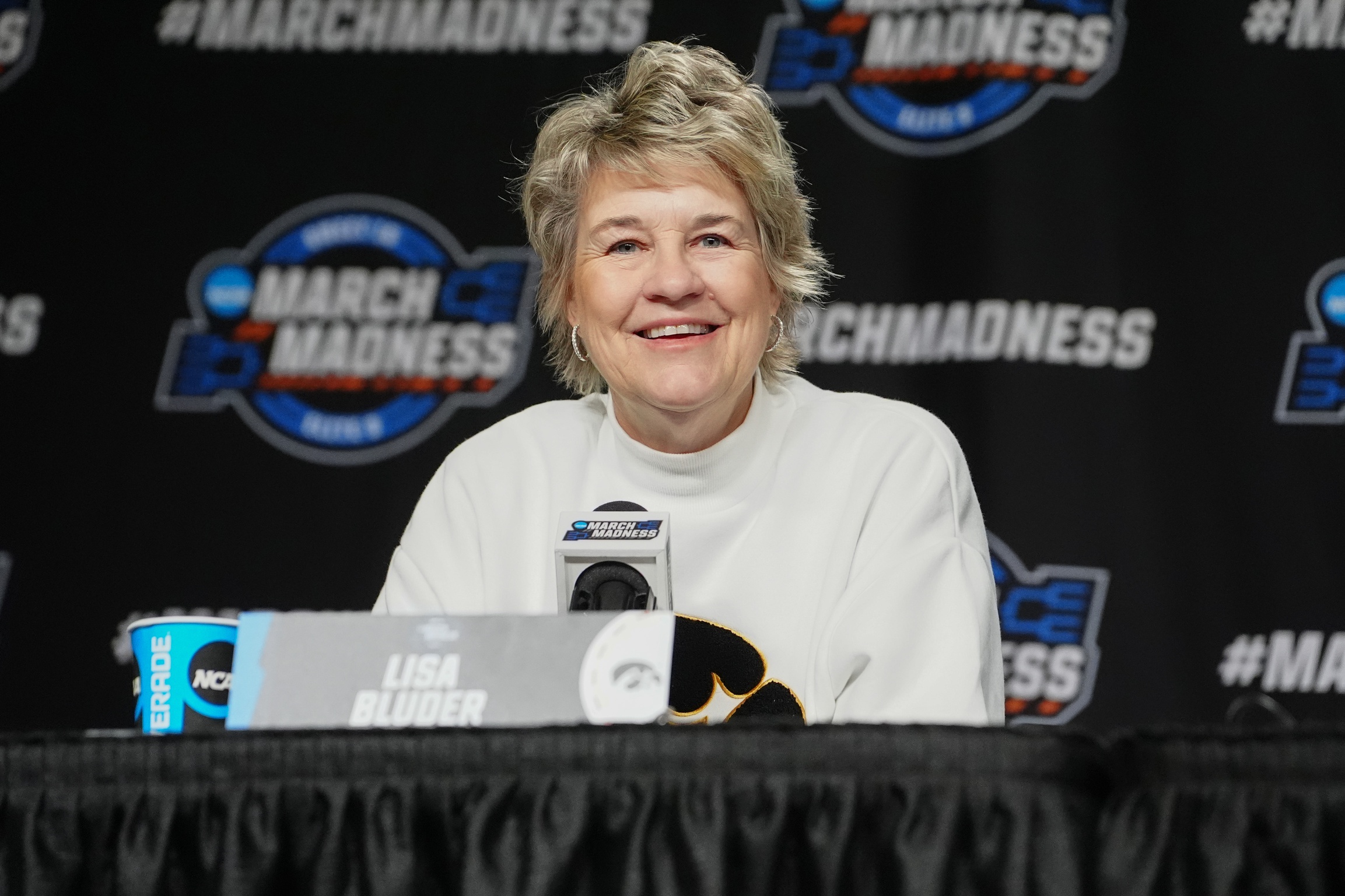 Lisa Bluder smiles as she speaks to media at a podium in Albany.