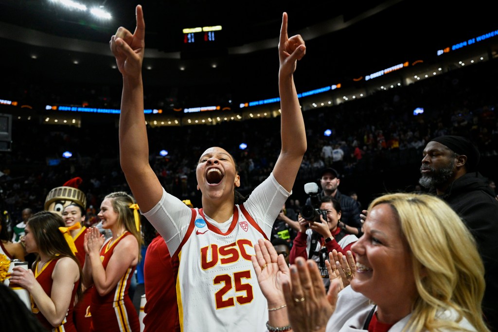 McKenzie Forbes points two fingers in the sky as she screams in celebration of USC's victory as cheerleaders and team personnel clap around her.