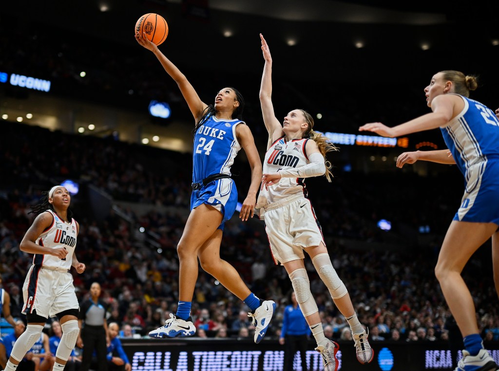 Reigan Richardson soars in the air lifting the basketball up toward the basket as Paige Bueckers jumps behind her trying to block the shot but not getting close.