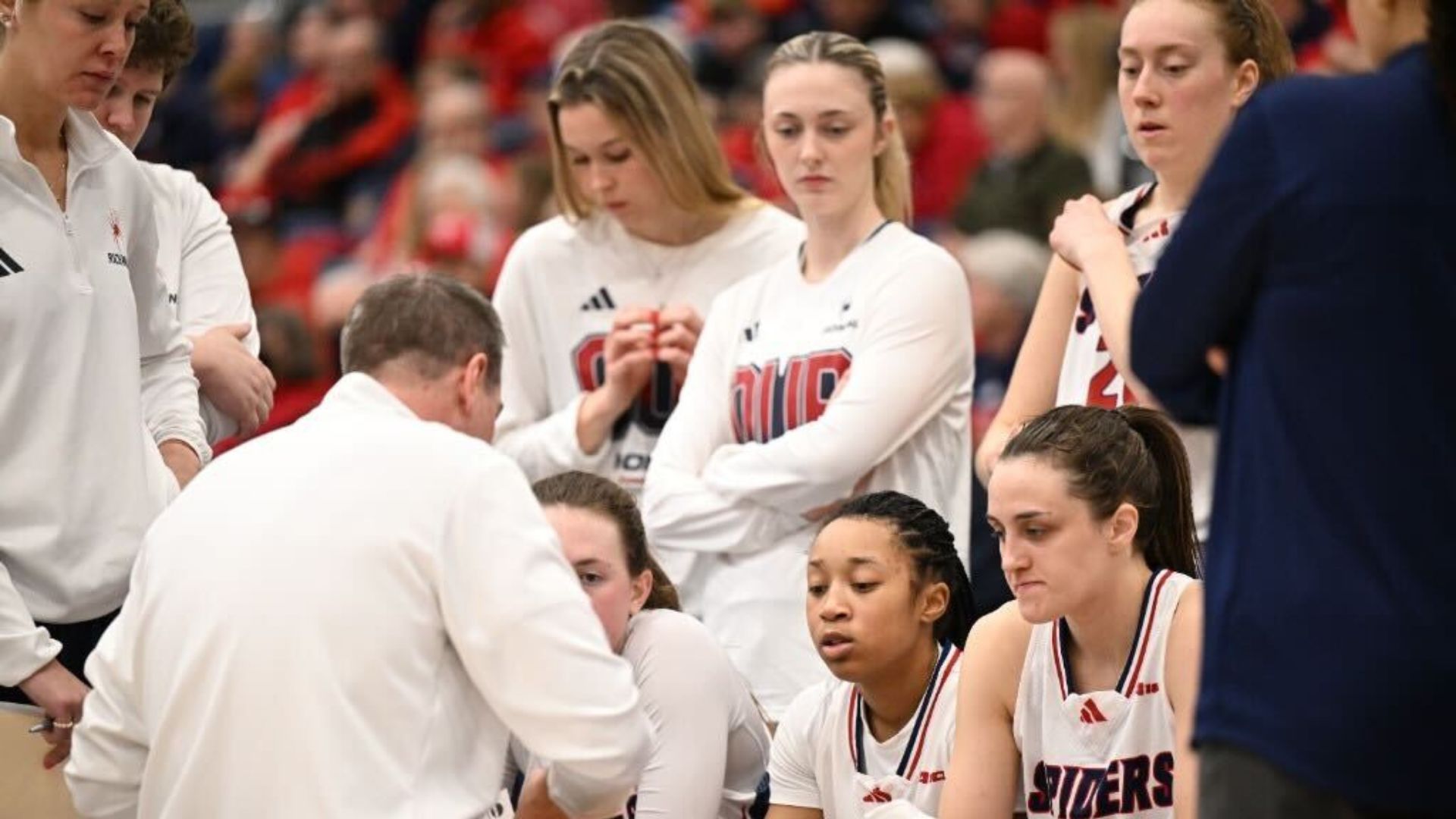 Richmond head coach Aaron Roussell draws up a play on a white board and is explaining to his team what he wants done out of the timeout. The team is focused on what he is saying.