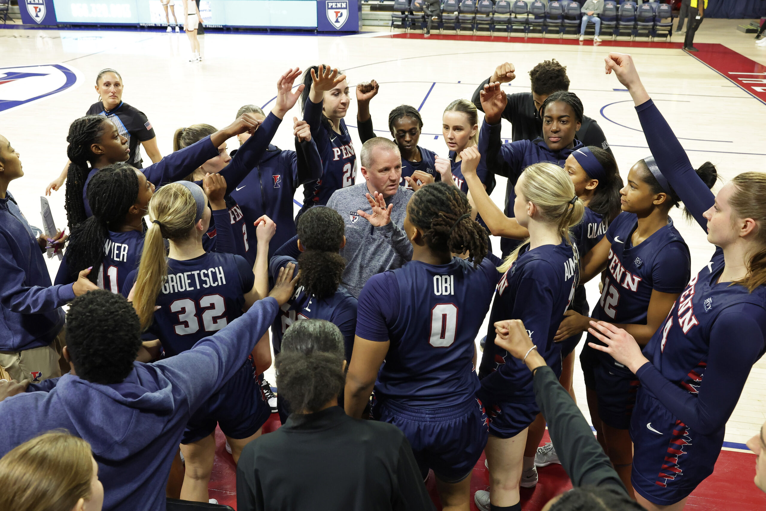 Penn women's basketball players put their hands together in a huddle.