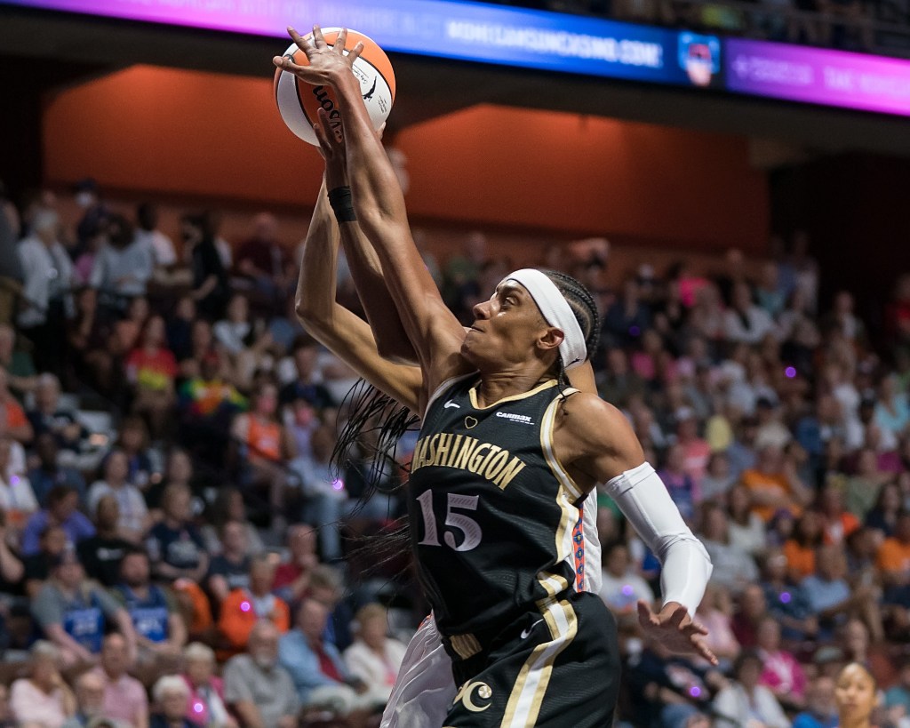 Washington Mystics guard Brittney Sykes jumps in stride with Connecticut Sun forward DeWanna Bonner and blocks Bonner's shot with her right hand.