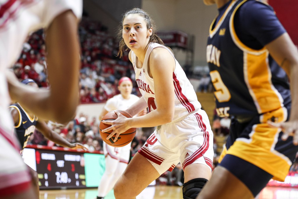 Mackenzie Holmes pivots while holding the basketball at hip height, players blurry in motion around her, a look of concentration on her face