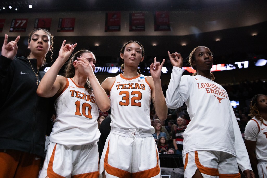 Four Texas players stand in a line holding up the Texas Longhorns hand signal with blank disappointed looks on their faces