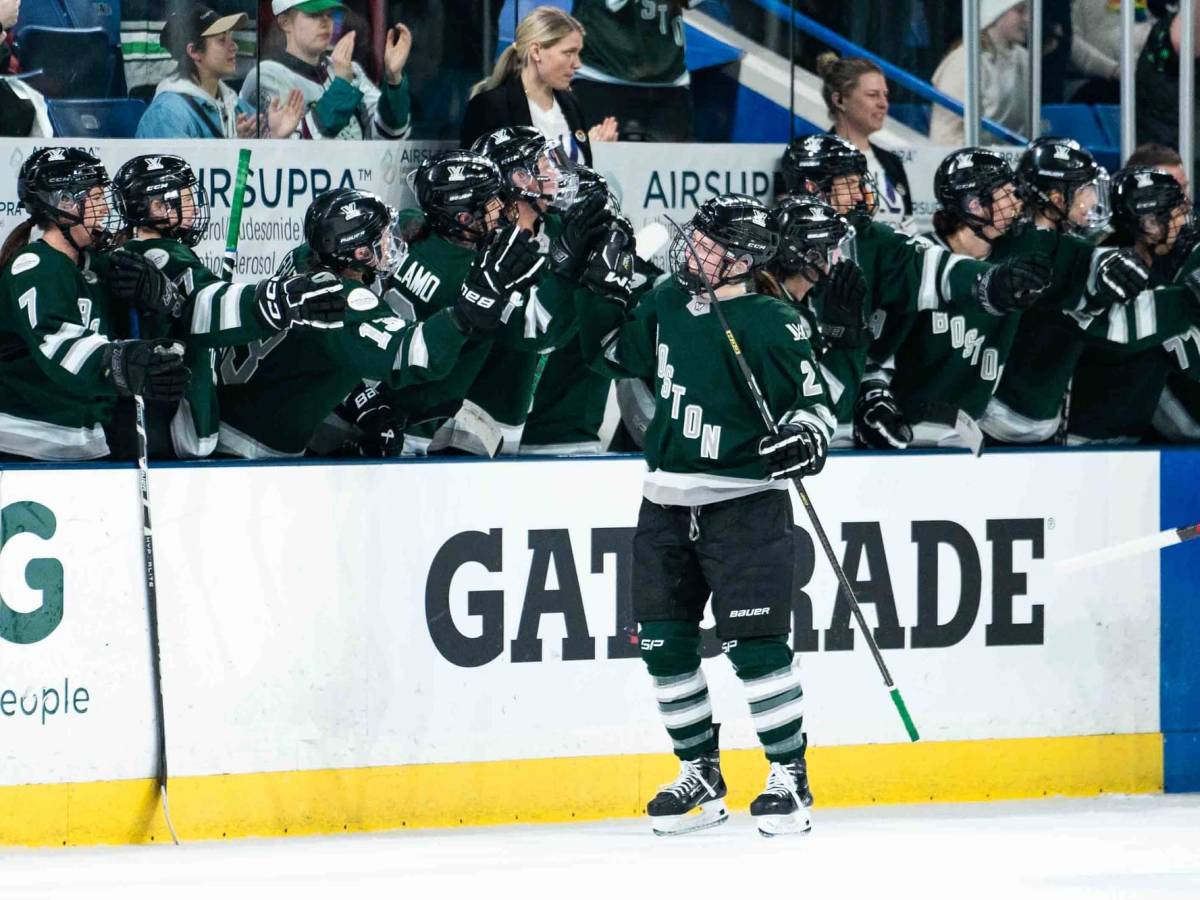 Emily Brown skates down and gets fist bumps at the bench to celebrate her first goal. She is wearing a green home uniform.