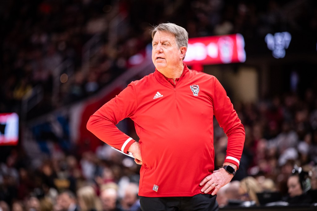 NC State head coach Wes Moore looks out on the court. His left hand is loosely resting on his hip, while is right hand is balled into a fist against his waist.