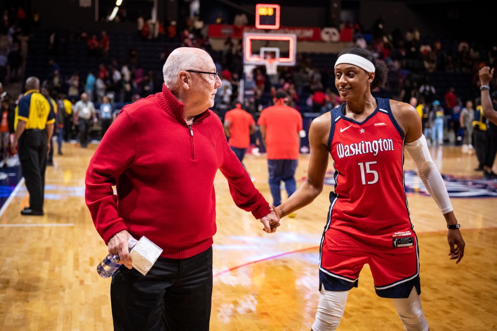 Washington Mystics guard Brittney Sykes high-fives general manager Mike Thibault as they walk off the court. Both are smiling and looking at each other.