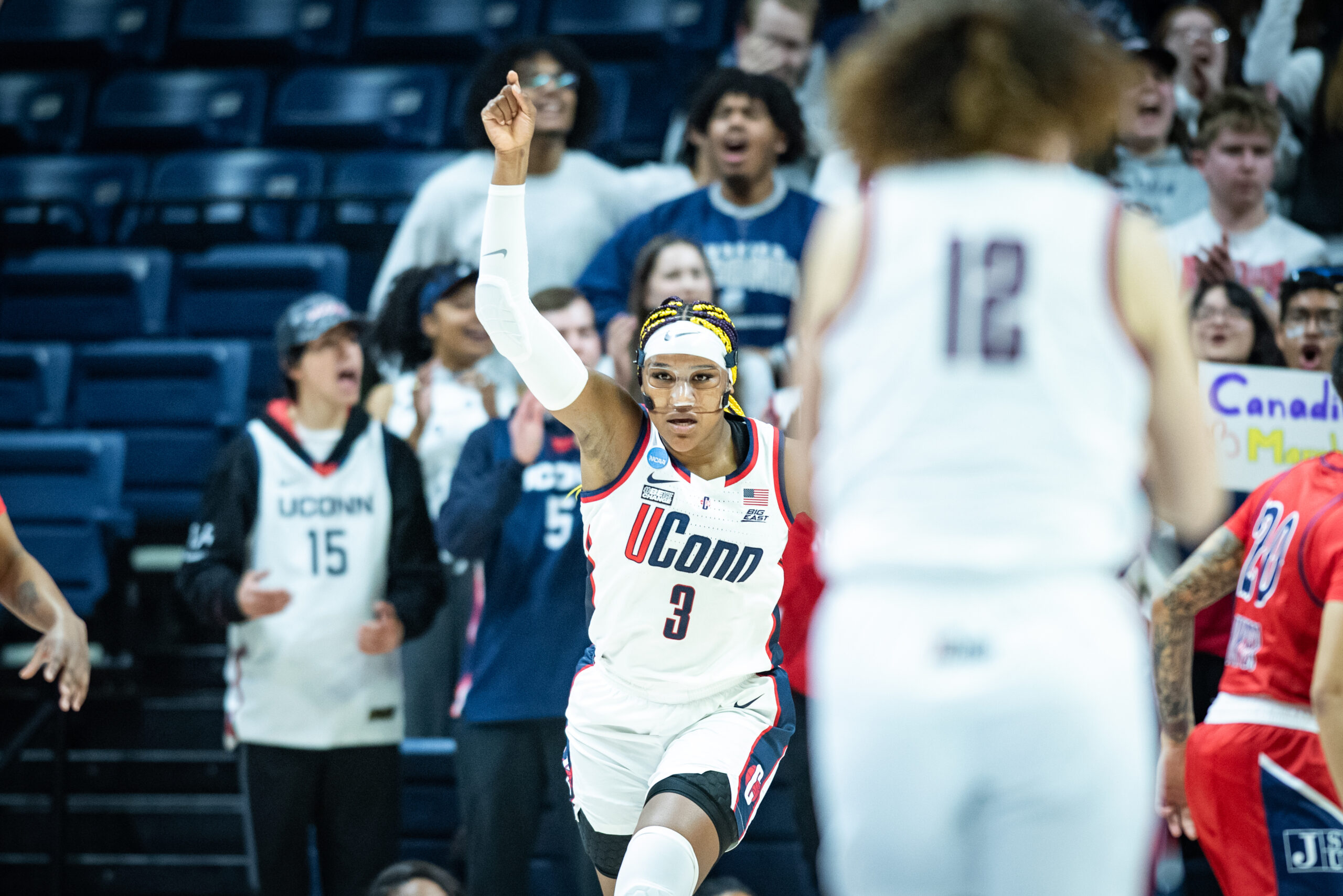 UConn forward Aaliyah Edwards holds her right arm in the air and points as she runs down the court.