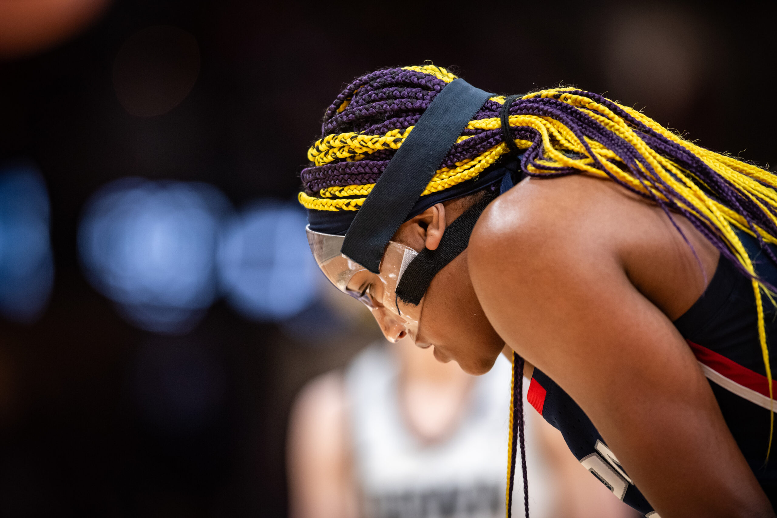 A masked Aaliyah Edwards is shown in profile, looking down at the floor.