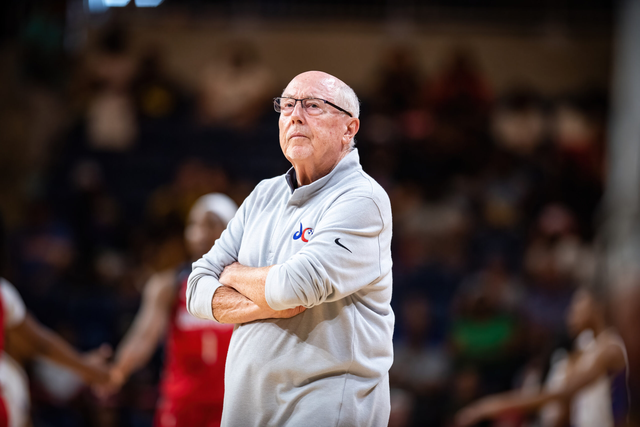 Washington Mystics general manager and then-head coach Mike Thibault stands with his arms crossed and a slight frown as he watches a game unfold.