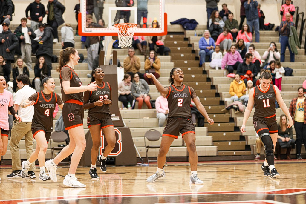Brown guard Kyla Jones pumps her right fist to celebrate a game-winning shot. Her teammates around her are beaming.