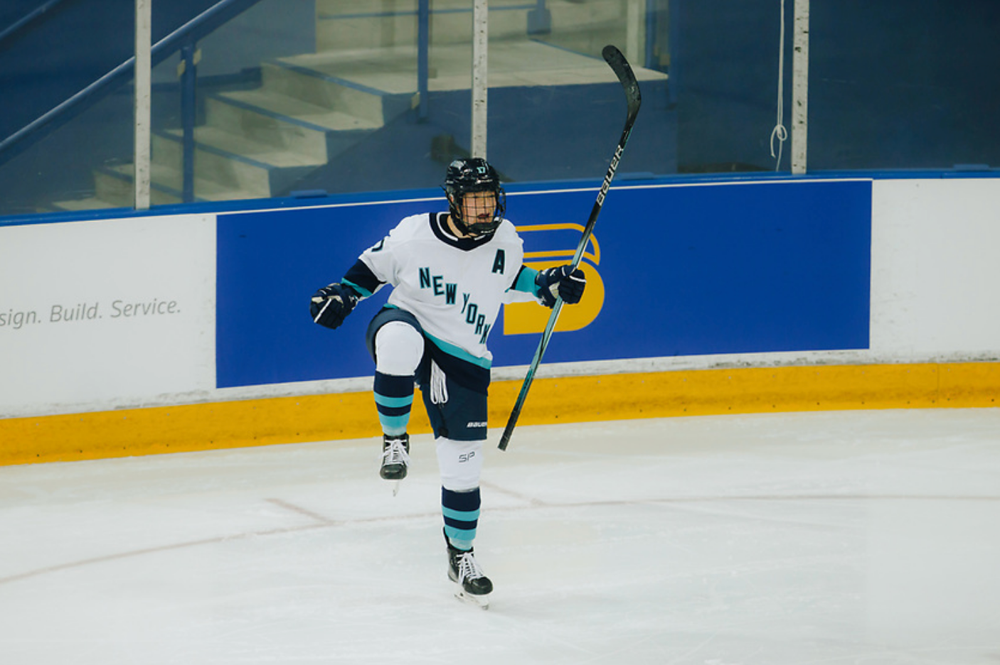 Ella Shelton celebrates a goal against Toronto. Her stick is raised in her left hand and both arms slightly raised and out to the sides. Her left leg is also raised in celebration. She is wearing a white away uniform.