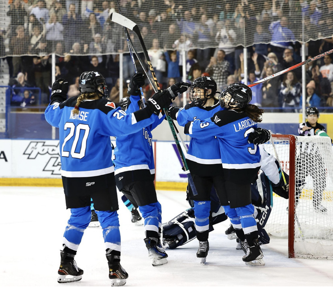 Nurse skates toward Spooner, Larocque, and another teammate with her arms open for a hug. Larocque and Spooner are already hugging, while another unidentifiable Toronto skater is also about to join in. All are in blue home uniforms.