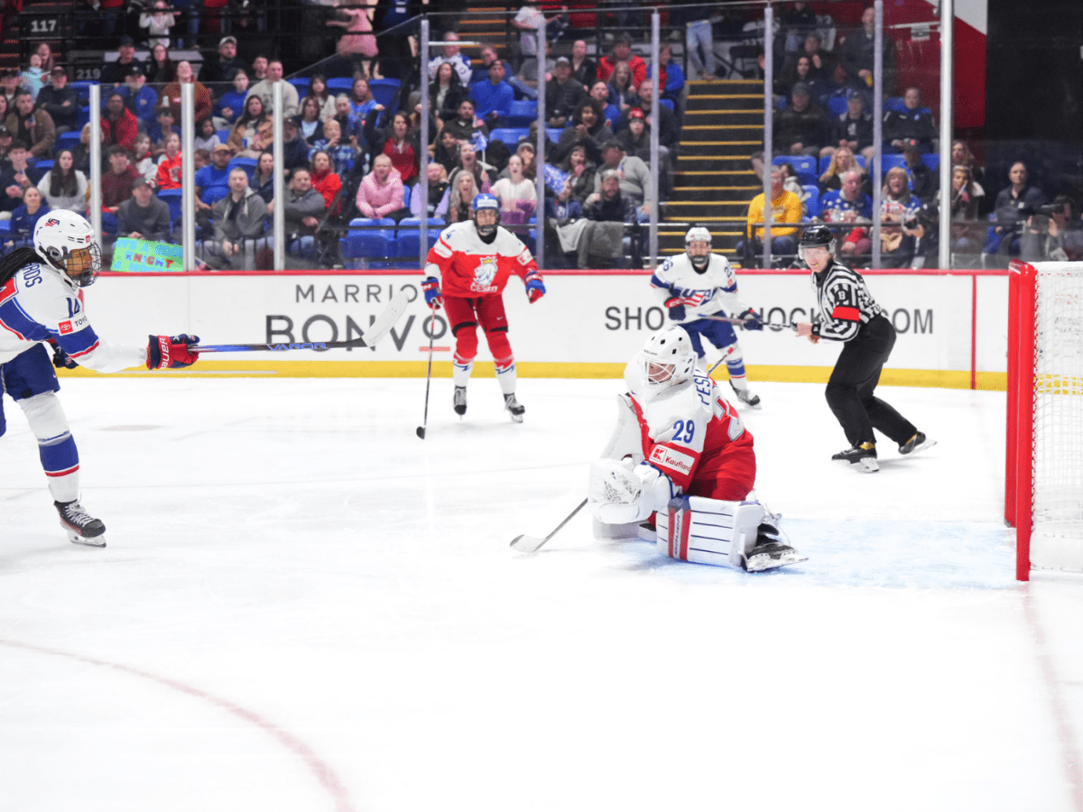 Edwards (far left) is following through the shot, while Peslarová (right) is on her knees. The puck is in the goal.
