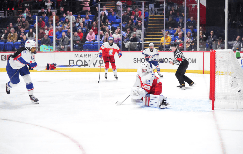 Edwards (far left) is following through the shot, while Peslarová (right) is on her knees. The puck is in the goal.