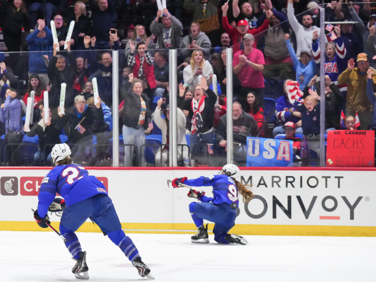 Simms fist pumps while on her knees to celebrate her overtime winner. Heise is to her left. Both are in blue.