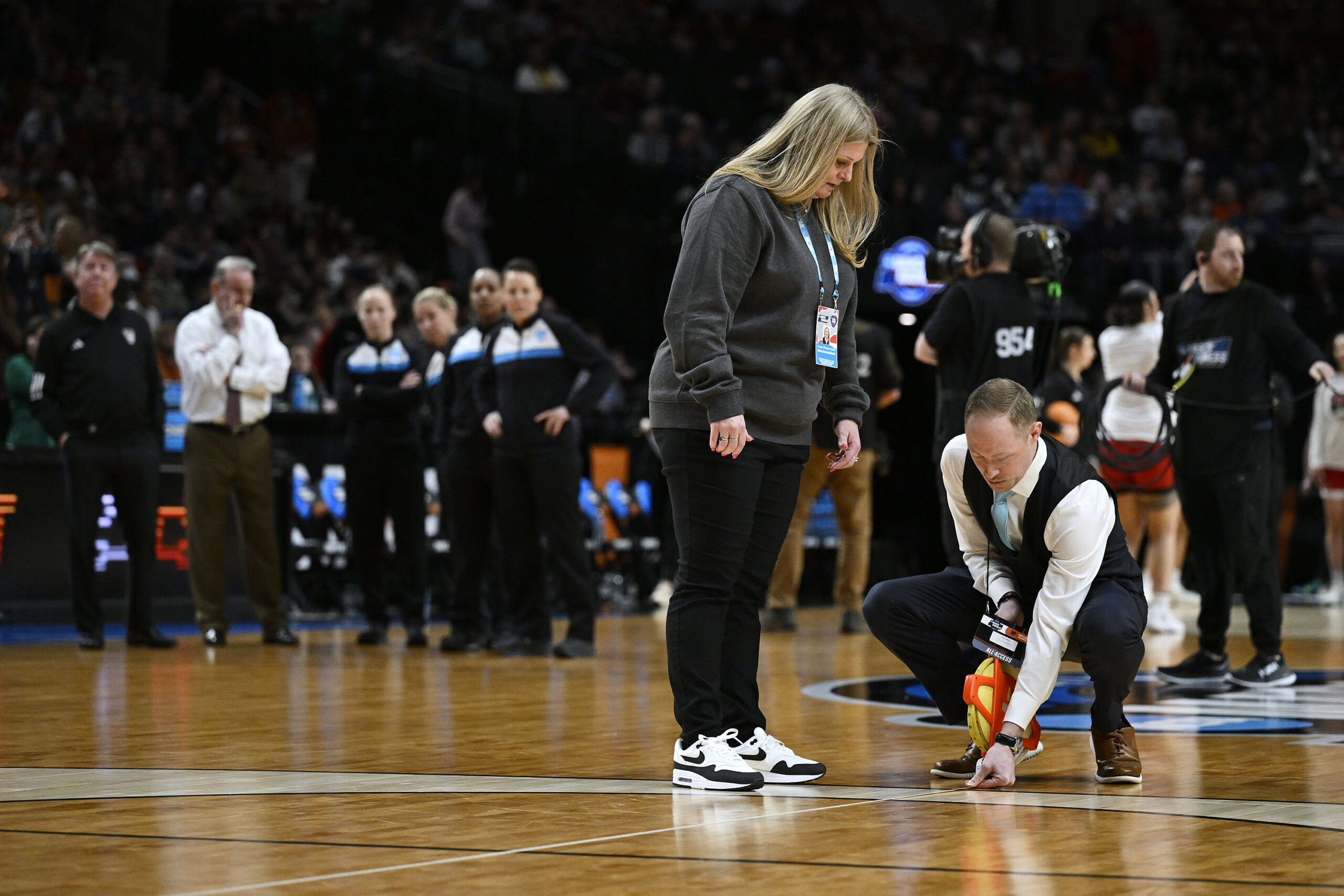 NCAA officials measure the 3-point arc on a basketball court