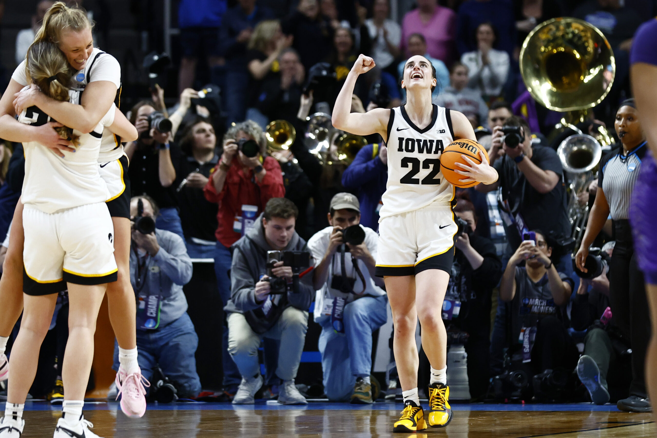 Caitlin Clark celebrates Elite Eight win while teammates embrace in foreground of photo