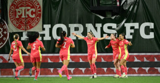 Portland Thorns teammates celebrate with a "Thorns" banner in the backdrop
