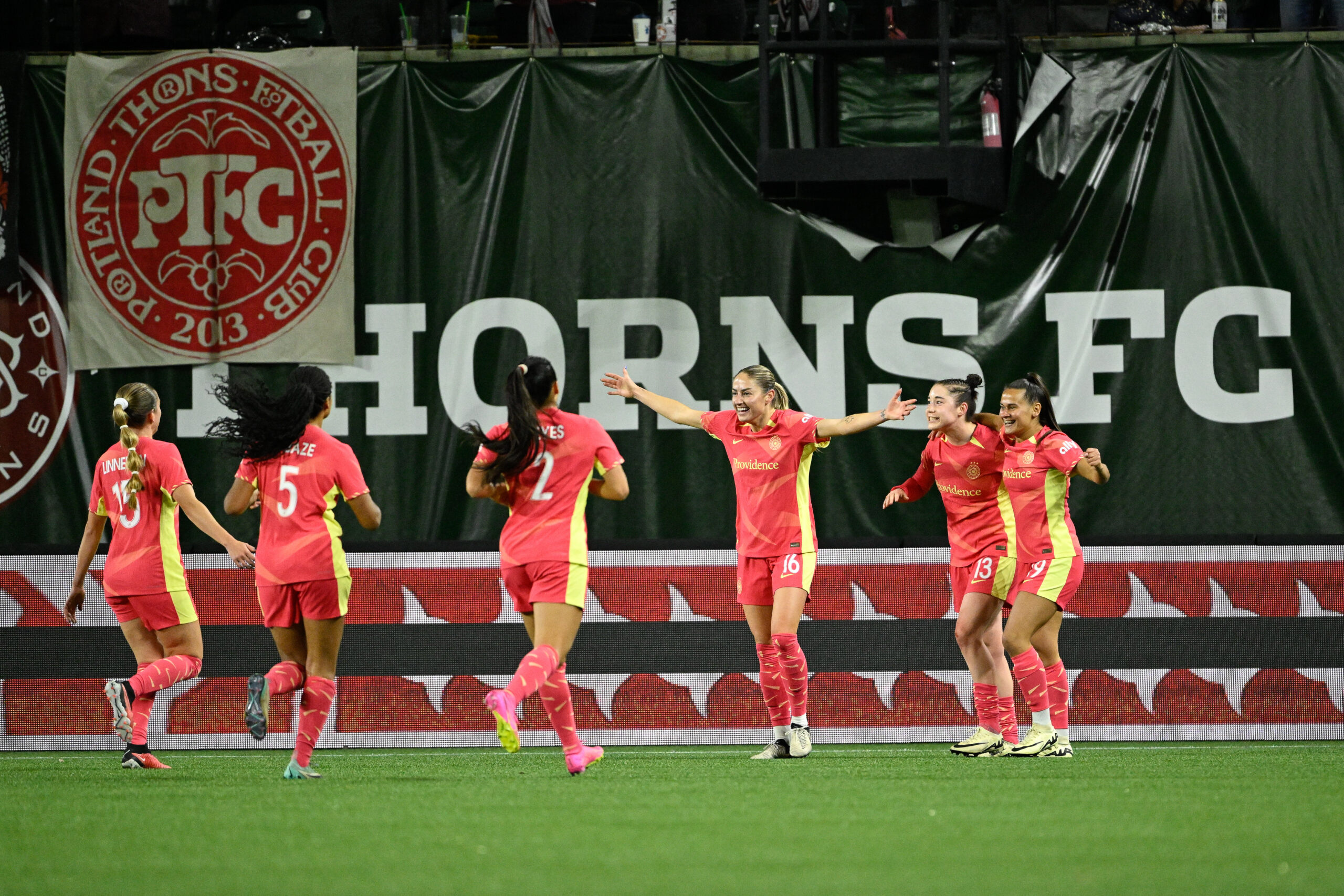 Portland Thorns teammates celebrate with a "Thorns" banner in the backdrop