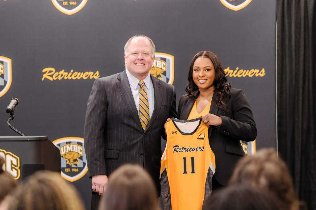 Rich Franchak (left) and Candice Hill (right) pose for a photo at her introductory press conference. She is holding a yellow jersey with "Retrievers" on it and the number 11.  