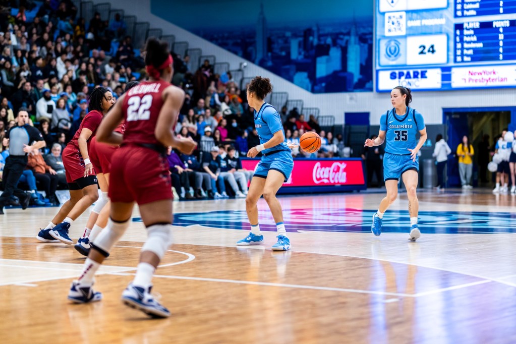 Columbia forward Kaitlyn Davis stands on the 3-point line near the top of the key. She flips the ball behind her back with her right hand to guard Abbey Hsu, who is trailing the play.