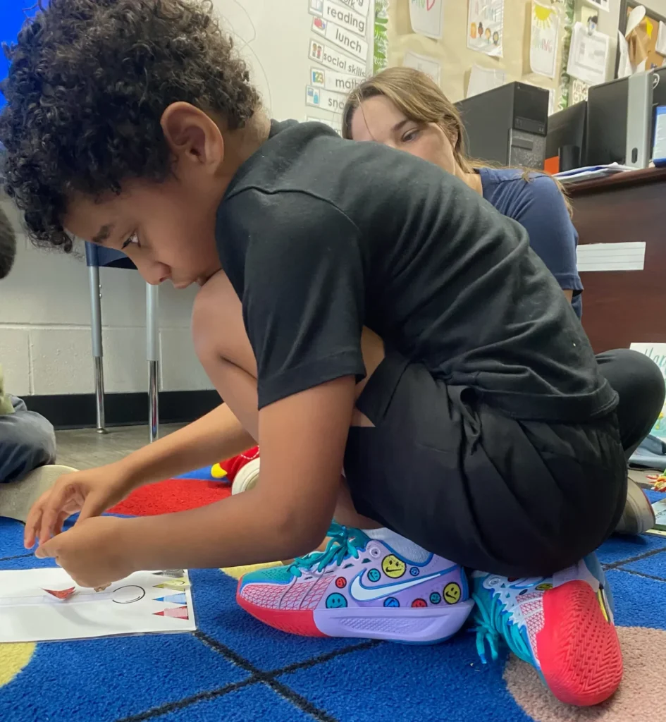Justice Swann making an art project on the ground while wearing Jewell Loyd’s player-edition sneakers