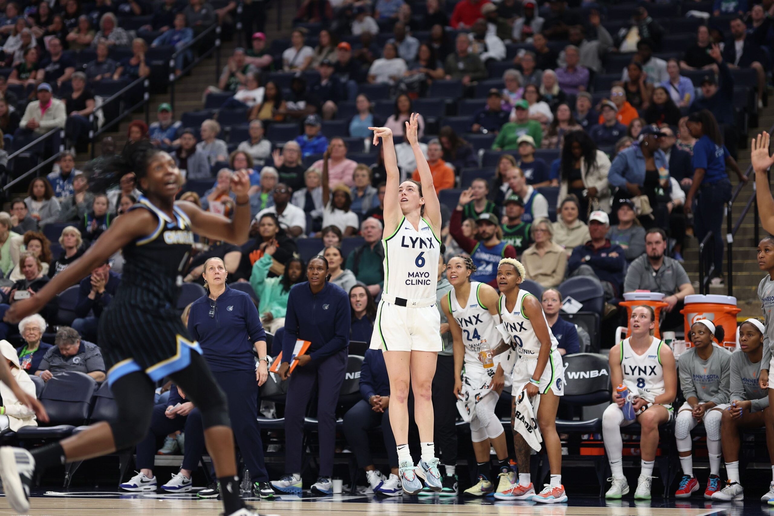 Minnesota Lynx forward Bridget Carleton shoots a jump shot in front of her bench. Two of her teammates stand in anticipation as they watch the flight of the ball.