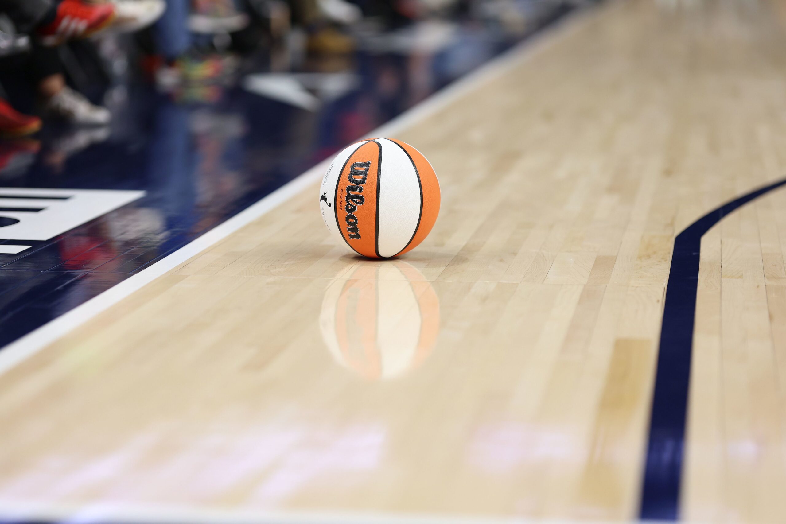 A WNBA ball rests on the court, with the Wilson logo visible and aligned perpendicular to the court.