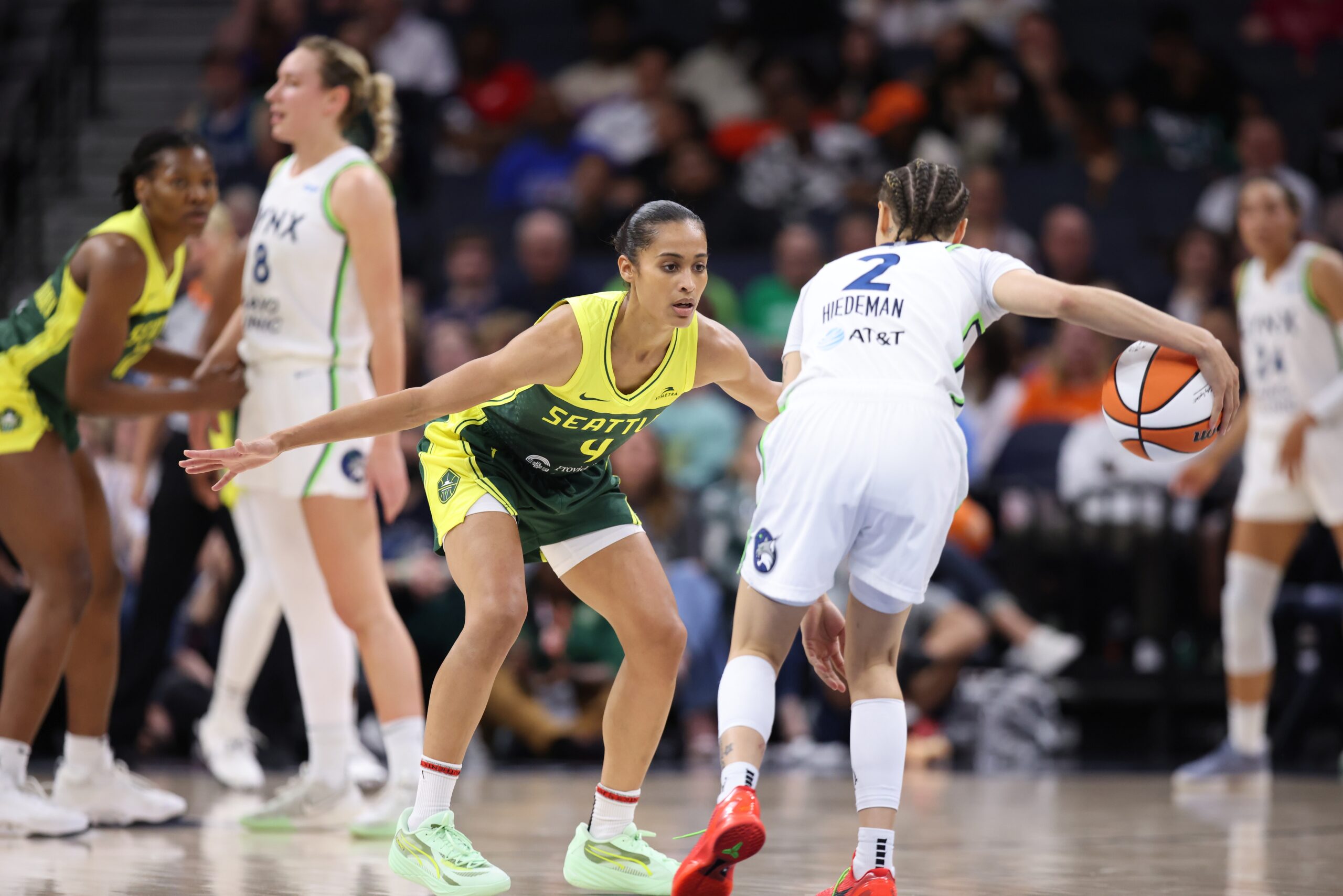 Seattle Storm point guard Skylar Diggins-Smith stands in a low defensive position with her arms out wide. She defends Minnesota Lynx guard Natisha Hiedeman, who is dribbling the ball.