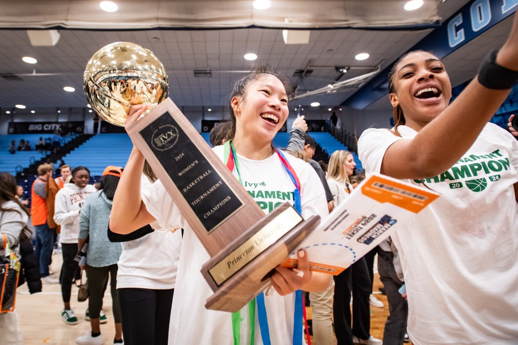 Princeton guard Kaitlyn Chen holds the Ivy League Tournament championship trophy, which looks nearly as big as her head and torso. She and her teammate Chet Nweke are both smiling.