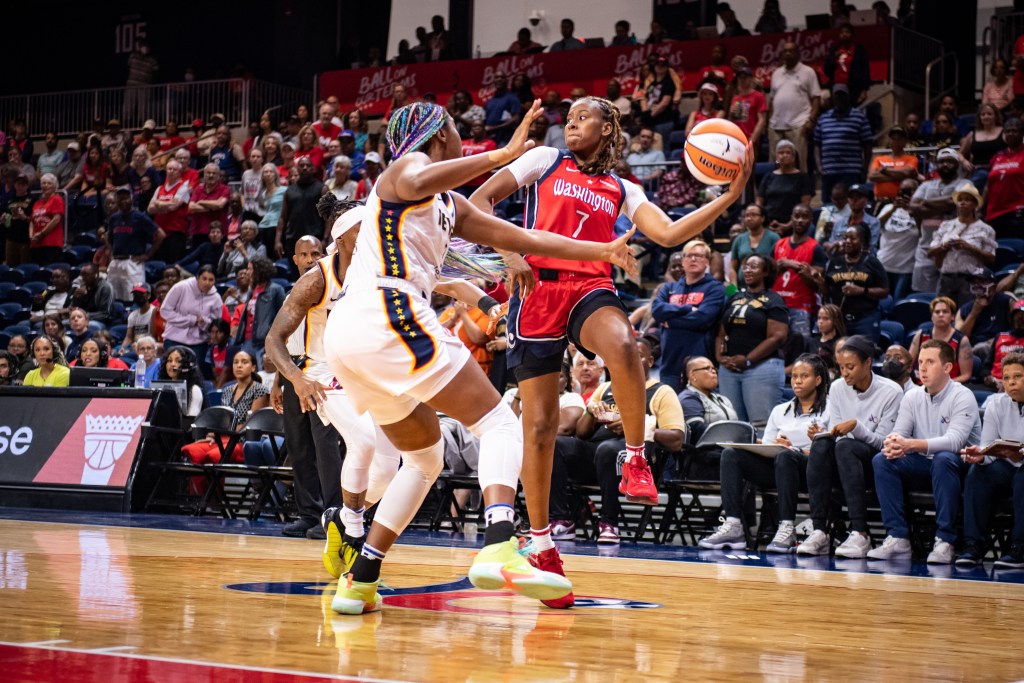 Washington Mystics guard Ariel Atkins jumps off her right foot and cradles the ball in her left hand, looking to pass over the defense.