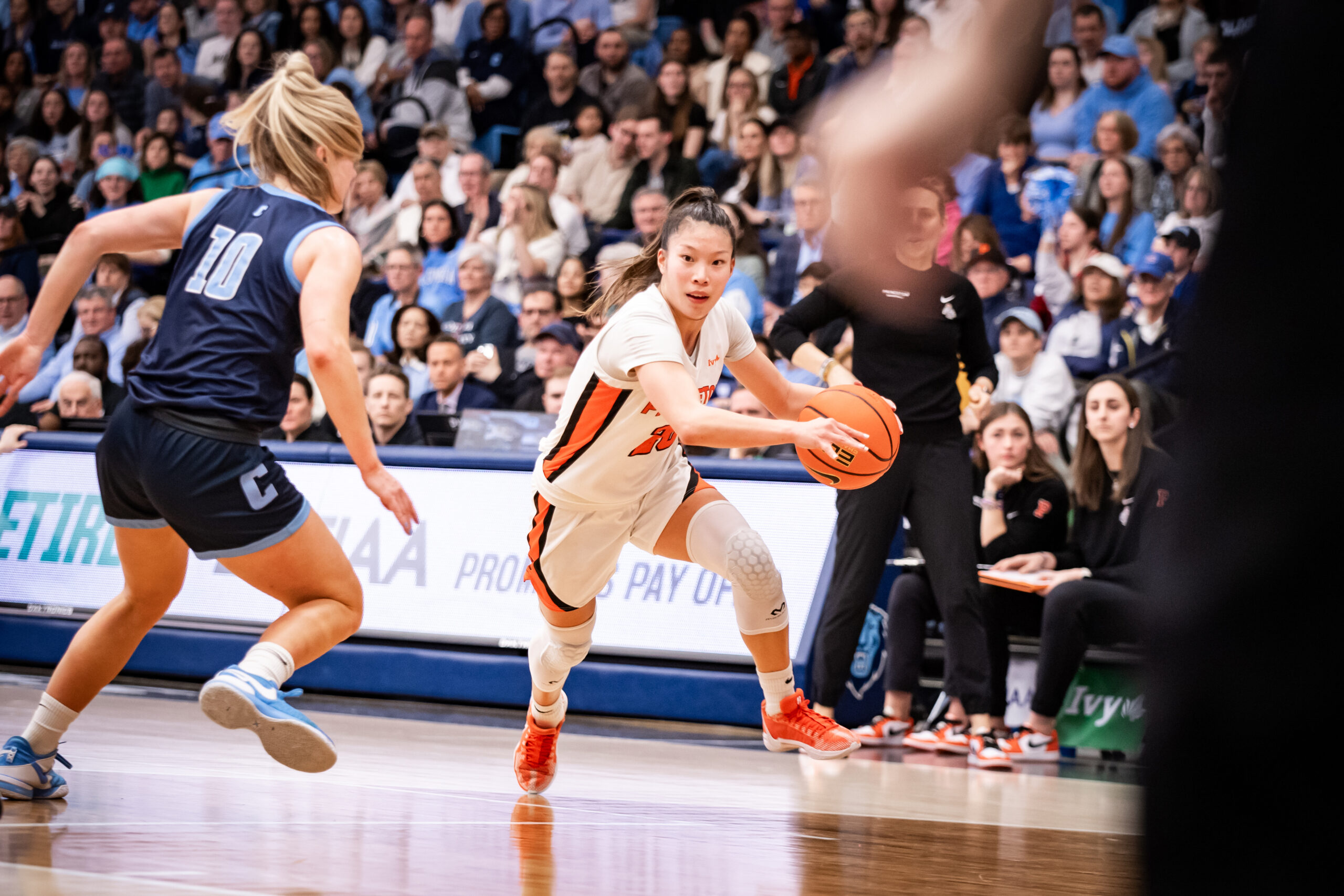 Princeton guard Kaitlyn Chen drives the ball with her left hand on the left side of the court. Columbia guard Kitty Henderson slides her feet diagonally to try to cut Chen off.