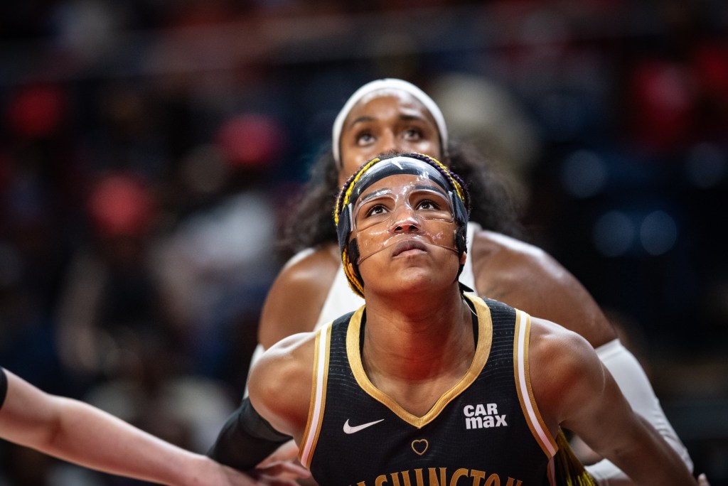 Washington Mystics forward Aaliyah Edwards stands directly in front of an Atlanta Dream player. Both players have their heads tilted upward as they watch the flight of the ball.