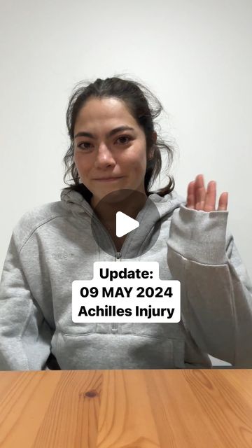 A screenshot of a video by Georgia Godwin of Australia. In the video, she wears a gray sweatshirt, sits at a table and waves to the camera with her left hand.