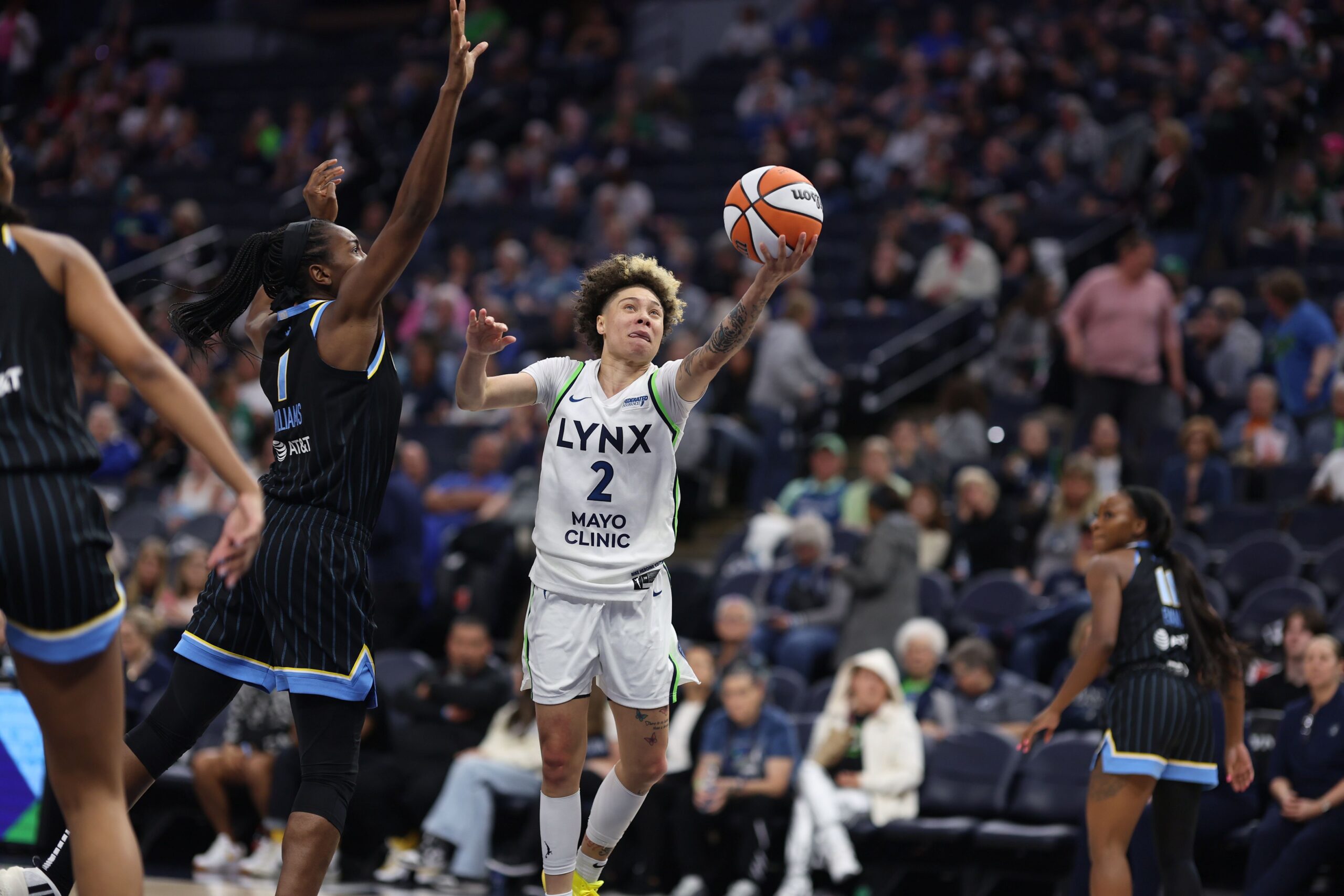 Minnesota Lynx guard Natisha Hiedeman cradles the ball while extending her arm to shoot a layup around the reach of Chicago Sky center Elizabeth Williams during a WNBA preseason game.